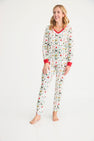A woman stands barefoot on a white background, smiling as she wears The Beaufort Bonnet Company’s Coastal Living Lounge Set - 12 Days of Christmas with Richmond Red, crafted from soft Pima Cotton pajama fabric and adorned with colorful holiday-themed patterns and red trim.