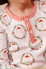 A child wearing The Beaufort Bonnet Company’s Sutton’s Sweet Dream Set - North Pole Portrait with Richmond Red Stripe, featuring a white shirt with a red striped collar and buttons, decorated with smiling Santa Claus faces framed by holly wreaths.