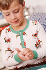 A young child in The Beaufort Bonnet Company’s Sutton’s Sweet Dream Set - Serious Santa Business kneads dough with both hands, focusing intently. The Pima cotton Christmas pajamas showcase playful Santa Claus designs, while the softly blurred background adds a gentle touch to the scene.