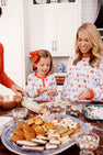 Wearing the Sutton’s Sweet Dream Set - Santa’s Laundry Line with Richmond Red pajamas from The Beaufort Bonnet Company, a woman and a young girl smile together as they decorate cookies in the kitchen, surrounded by baking tools, sprinkles, and an assortment of cookies spread out on the counter.