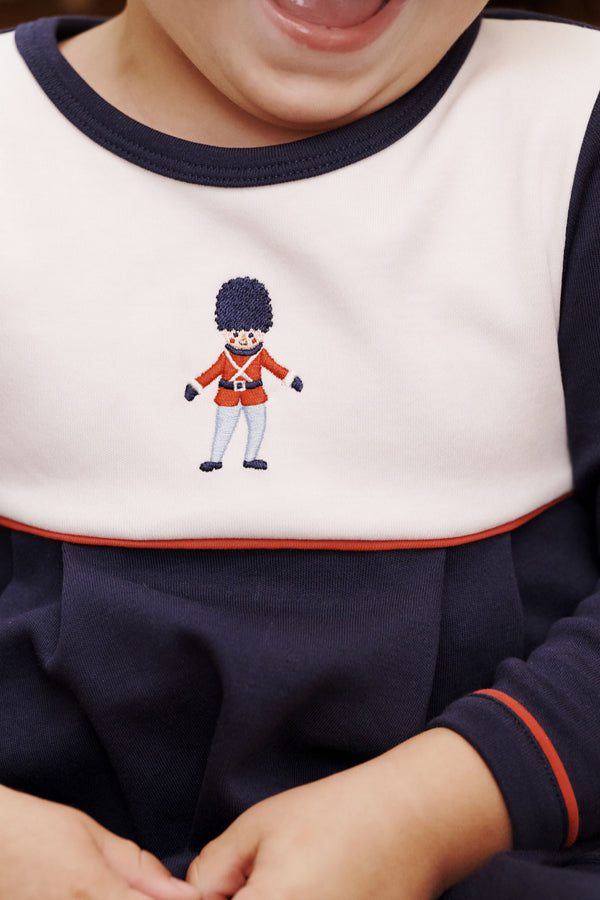 Close-up of a child in a navy and white Long Sleeve Bradford Romper - Nantucket Navy & Worth Avenue White with Soldier Embroidery featuring an embroidered toy soldier on the chest.