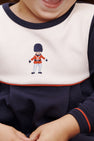 Close-up of a child in a navy and white Long Sleeve Bradford Romper - Nantucket Navy & Worth Avenue White with Soldier Embroidery featuring an embroidered toy soldier on the chest.
