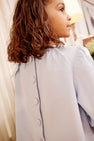 A young girl with curly brown hair is standing indoors, looking to the side, wearing The Beaufort Bonnet Company’s Dani Dress in Buckhead Blue Corduroy with buttons down the back.