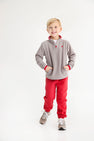 A young boy in a cozy Hayword Half-Zip (Fleece) - Grantley Gray with Richmond Red and matching sweatpants stands with his hands in his pockets.
