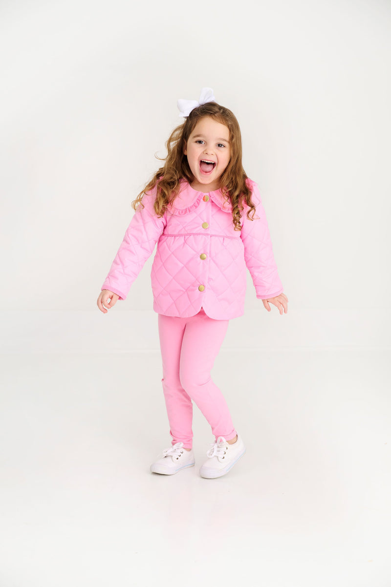 A young girl wearing a quilted jacket and matching Mitzy Sue Slacks (2-Pack) - Hamptons Hot Pink smiles excitedly.
