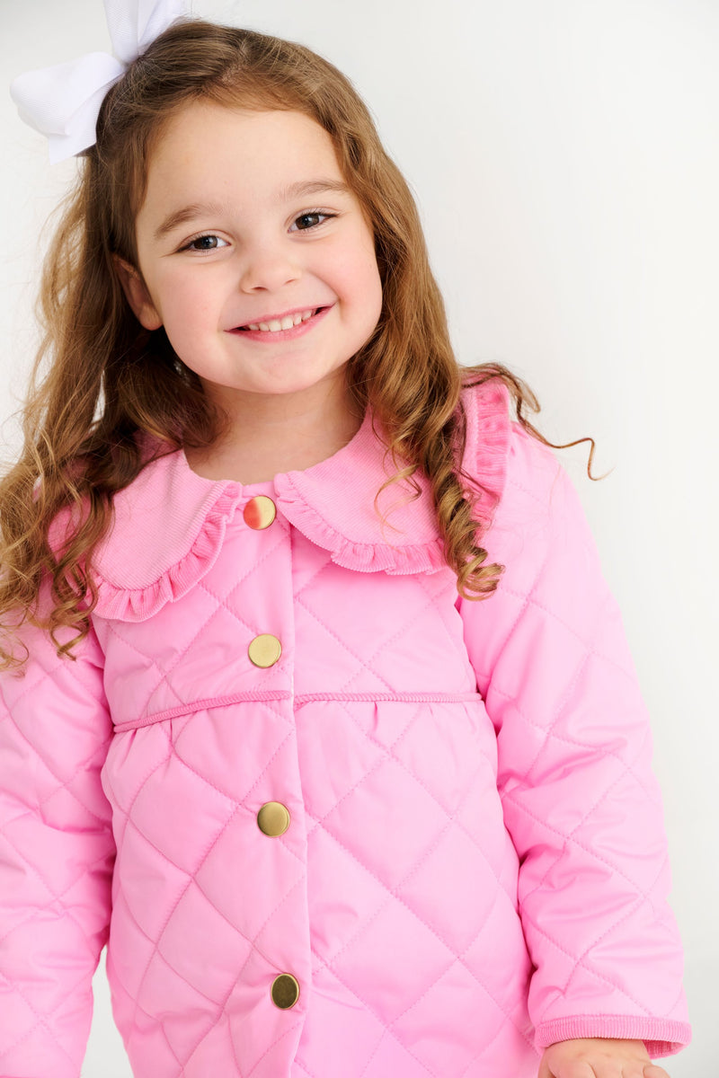 A young girl smiles wearing a bright pink Maude’s Carlyle Quilted Coat - Hamptons Hot Pink with Palm Beach Pink, featuring a ruffled collar and gold buttons.
