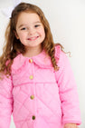 A young girl smiles wearing a bright pink Maude’s Carlyle Quilted Coat - Hamptons Hot Pink with Palm Beach Pink, featuring a ruffled collar and gold buttons.