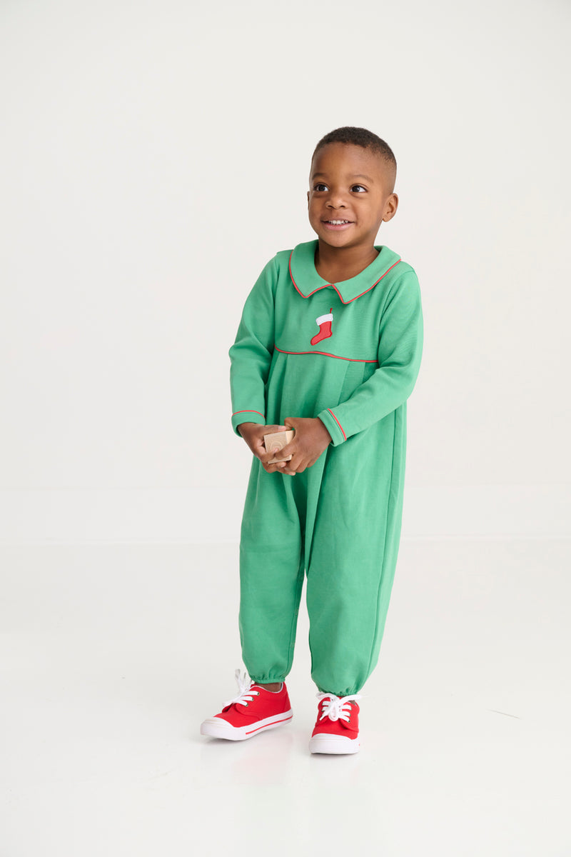 A young child stands in a Long Sleeve Bradford Romper—Kiawah Kelly Green with Stocking Embroidery by The Beaufort Bonnet Company, paired with red shoes and holding a small object, against a plain white background.
