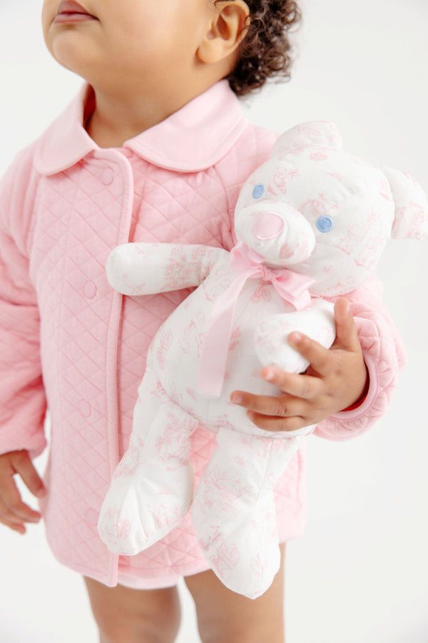 A toddler wearing The Beaufort Bonnet Company’s Sir Proper’s Sweet Arrival (Hamptons Hot Pink) Bundle - Adorable Everyday Set holds the charming Bradley Bear, complete with pink patterns and a pink bow—an irresistible scene that makes a delightful baby shower gift. The child’s face is partially visible against a simple white background.