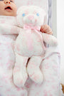 A baby lies in a crib, nestled in The Beaufort Bonnet Company’s Sir Proper’s Sweet Arrival (Hamptons Hot Pink) Bundle – Adorable Everyday Set & Bradley Bear. The soft bedding and the cuddly Bradley Bear, both featuring coordinating light pink patterns, create a charming scene that’s perfect for welcoming a newborn or giving as an elegant baby shower gift.