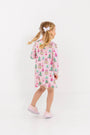 A young girl wearing a Long Sleeve Polly Play Dress - Christmas Coloring Contest, a long-sleeve Pima cotton dress printed with festive snow globes and trees.