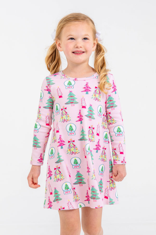 A young girl wears a long-sleeved, pink Long Sleeve Polly Play Dress - Christmas Coloring Contest in Pima cotton, printed with colorful trees and snow globes.