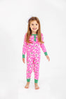 A young girl with long hair is smiling against a plain white background, wearing The Beaufort Bonnet Company’s Sara Jane’s Sweet Dream Set - Bows of Holly with Kiawah Kelly Green, a pink holiday family matching pajama set.