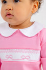 Close-up of a baby wearing a Rigsby Romper - Hamptons Hot Pink with Worth Avenue White and Bow Smocking, featuring a white Peter Pan collar and white bow smocking across the chest.