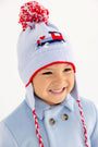 A smiling child wears The Beaufort Bonnet Company’s Parrish Pom Pom Hat in Beale Street Blue with a playful train motif, complete with ear flaps, red trim, and a red-and-white pompom.