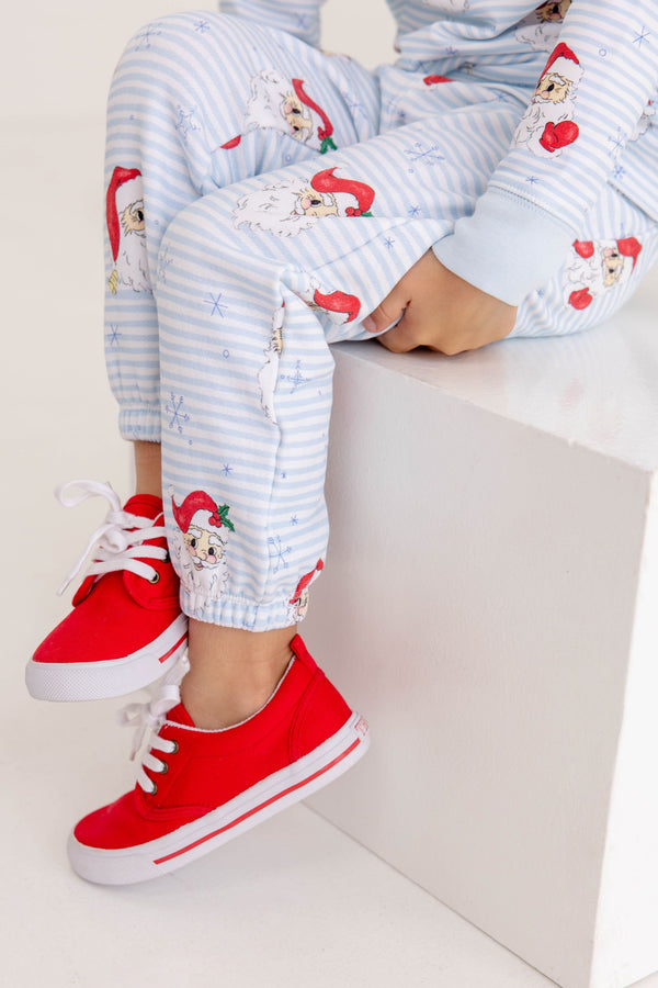 A person wears Gates Sweeney Sweatpants - Dear Santa (Buckhead Blue Stripe) and red sneakers while sitting on a white cube.