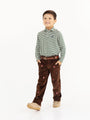 A smiling young boy stands with his hands in his pockets against a white background, wearing The Beaufort Bonnet Company’s Long Sleeve Prim & Proper Polo & Onesie in Grier Green & Palmetto Pearl Stripe with Nantucket Navy Stork. Styled with brown pants featuring small red designs, a matching brown belt, and beige shoes, his preppy outfit is perfect for any occasion.