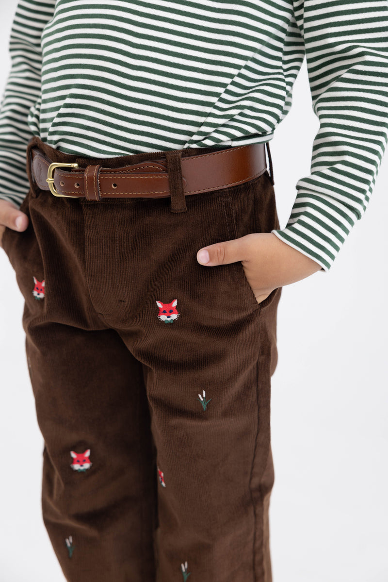 A child wears a green and white striped shirt, The Beaufort Bonnet Company Critter Prep School Pants in Chelsea Chocolate Corduroy with Fox Embroidery, and a brown belt. Their hands are in their pockets.