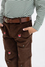 A child wears a green and white striped shirt, The Beaufort Bonnet Company Critter Prep School Pants in Chelsea Chocolate Corduroy with Fox Embroidery, and a brown belt. Their hands are in their pockets.