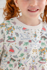 A smiling child with red hair wears The Beaufort Bonnet Company’s Cassidy Comfy Crewneck – 12 Days of Christmas, a quilted sweater adorned with colorful animal, musical instrument, and holiday-themed illustrations. Only the lower half of the child’s face and the top portion of the sweater are visible.