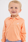 A smiling young child wearing The Beaufort Bonnet Company’s Long Sleeve Prim & Proper Polo & Onesie in Seashore Sherbet with a multicolor stork logo on the chest, standing against a plain white background.