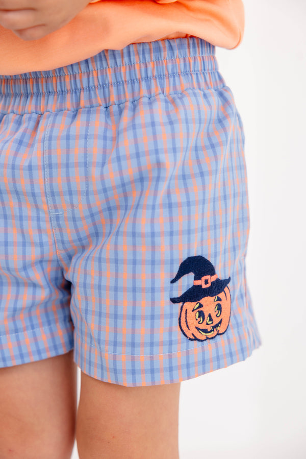A child wears The Beaufort Bonnet Company’s Sheffield Shorts in Wheaton Windowpane, adorned with a Seashore Sherbet Stork & Pumpkin Applique, paired with an orange shirt.