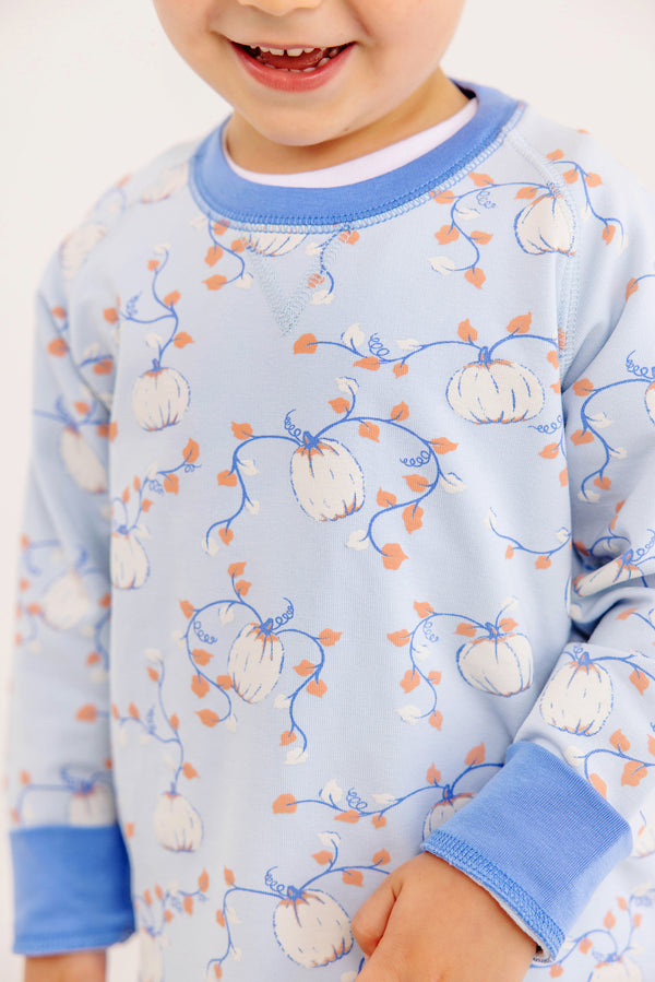A smiling child wears The Beaufort Bonnet Company Cassidy Comfy Crewneck – Gourd-geous (Buckhead Blue) with Sunrise Blvd Blue, featuring a white, orange, and blue pumpkin and vine design. Only the lower half of the face and upper body are visible.