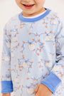 A smiling child wears The Beaufort Bonnet Company Cassidy Comfy Crewneck – Gourd-geous (Buckhead Blue) with Sunrise Blvd Blue, featuring a white, orange, and blue pumpkin and vine design. Only the lower half of the face and upper body are visible.
