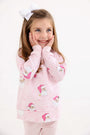 A girl wearing a Cassidy Comfy Crewneck - Dear Santa (Palm Beach Pink Stripe) with Palm Beach Pink, a long-sleeved crewneck decorated with Santa Claus illustrations and snowflakes.