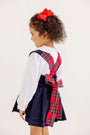 A young girl wears a Pearl Prep Skirt - Nantucket Navy Corduroy with Society Prep Plaid, a corduroy jumper featuring plaid straps that cross in the back and a large bow at the waist.