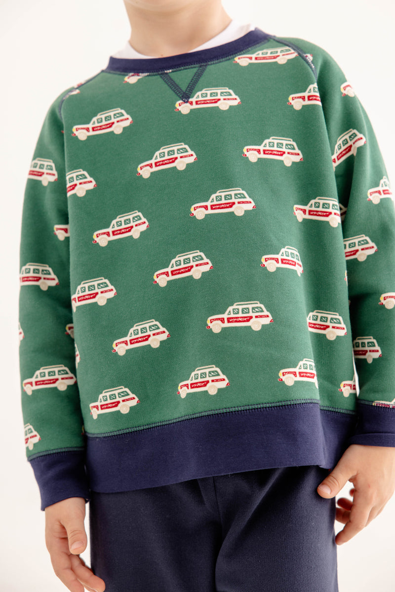 A child wears The Beaufort Bonnet Company’s Smitty Sweatshirt in Windsor Wagon (Grier Green) with Nantucket Navy, featuring a repeating red and white car print, navy cuffs, and a cozy fleece interior, paired with navy pants. The child’s face is not visible.
