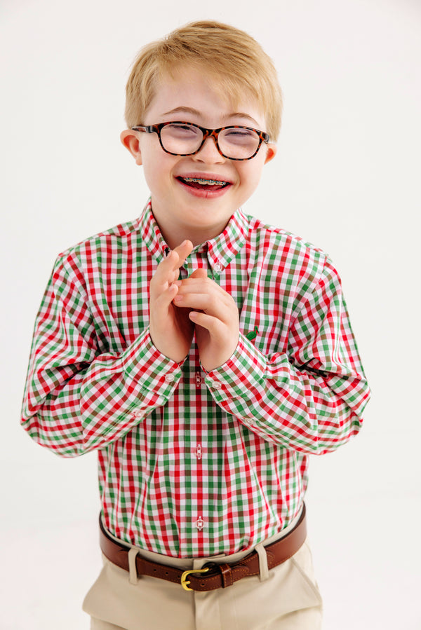 A smiling boy with glasses and braces, wearing The Beaufort Bonnet Company’s Dean’s List Dress Shirt in Richmond Red & Kiawah Kelly Green Gingham and khaki pants, stands against a plain white background.