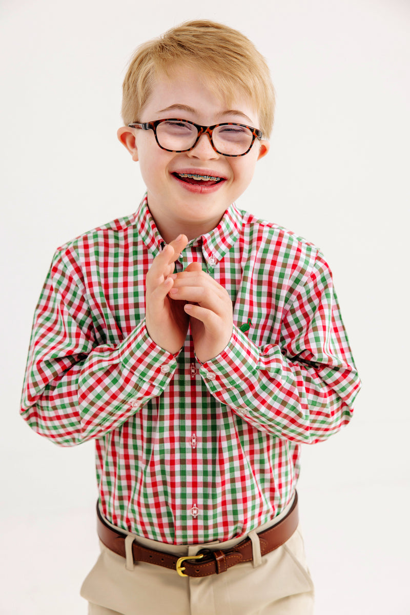 A smiling boy with glasses and braces, wearing The Beaufort Bonnet Company’s Dean’s List Dress Shirt in Richmond Red & Kiawah Kelly Green Gingham and khaki pants, stands against a plain white background.