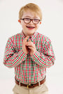 A smiling boy with glasses and braces, wearing The Beaufort Bonnet Company’s Dean’s List Dress Shirt in Richmond Red & Kiawah Kelly Green Gingham and khaki pants, stands against a plain white background.