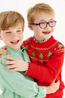 Two young boys smiling and hugging. One wears a green checkered shirt, the other is dressed in The Beaufort Bonnet Company’s “Isaac’s Fair Isle Sweater” in Richmond Red with Christmas Trees, along with glasses and braces. Both have light hair and look happy against a white background, while the festive cotton sweater adds warmth to the joyful scene.