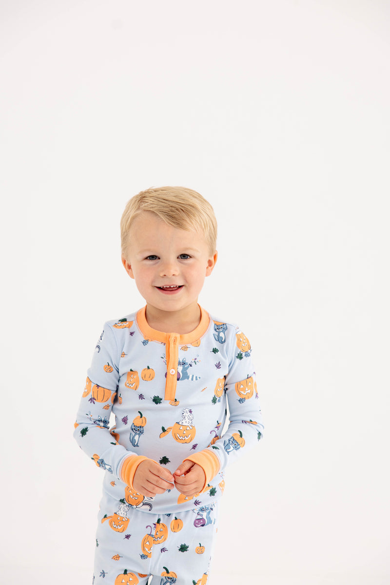 A young child with blonde hair is wearing The Beaufort Bonnet Company’s Payton Pajama Set – Candy & Critters (Buckhead Blue) with Seashore Sherbet, smiling against a plain white background.