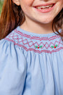 The Long Sleeve Sandy Smocked Dress - Barrington Blue with Richmond Red Holly is a light blue long-sleeve Christmas smocked dress featuring red and white holly berry and leaf patterns across the chest.