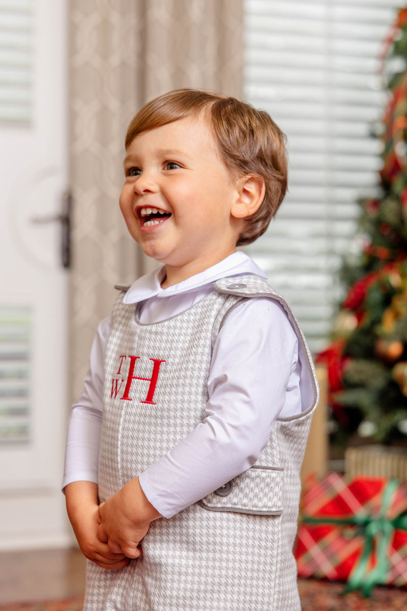 A smiling toddler wears a Jack Keene Jon Jon - Grantley Gray Houndstooth with Grantley Gray over a white collared shirt, featuring the monogram TWH embroidered in red, perfect for a winter family portrait.