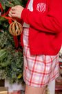 A person wearing a red cardigan and a Perrin Skirt - Broadway Play Plaid holds a gold glittery Christmas ornament.