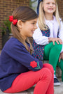 A girl in a navy Cassidy Comfy Crewneck - Nantucket Navy with Flowers with an embroidered flower patch on the elbow and red leggings sits outdoors next to a smiling girl in a floral vest and green leggings.