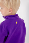 A young child with short blond hair, facing away from the camera, wears The Beaufort Bonnet Company’s LSU Hayword Half-Zip in LSU Purple with LSU Gold. A small yellow bird logo is visible near the collar on the back of the jacket.