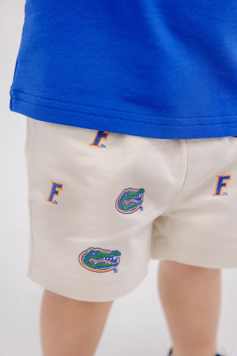 A child wearing The Beaufort Bonnet Company Florida Critter Sheffield Shorts - Saratoga Stone, paired with a blue shirt. The image highlights the lower back and legs, showing only part of the shirt and the kids’ gameday shorts.
