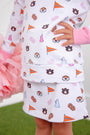 A child wearing The Beaufort Bonnet Company’s Auburn Searcy Skort in the Tiger Thrill print with Worth Avenue White, featuring Auburn University logos, tiger faces, pennants, pom-poms, and pink science beakers. The child holds pink pom-poms and stands on green grass, with only their torso and legs visible.