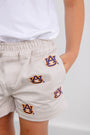 A child wearing The Beaufort Bonnet Company Auburn Critter Sheffield Shorts in Saratoga Stone, adorned with multiple Auburn University logos, stands with one hand in their pocket and a white shirt.