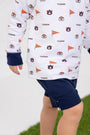 A child wearing The Beaufort Bonnet Company’s Auburn Cassidy Comfy Crewneck - Tiger Thrill with Auburn Blue and navy blue shorts stands on grass, with only the lower torso and legs visible.