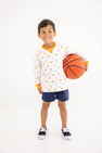 A smiling young boy stands against a plain white background, holding a basketball under one arm and wearing The Beaufort Bonnet Company’s Tennessee Cassidy Comfy Crewneck - Victory in Orange with Tennessee Orange and navy shorts.