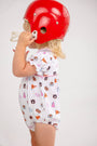 A young child wearing The Beaufort Bonnet Company’s Auburn Britt Bubble - Tiger Thrill with Hamptons Hot Pink, crafted from soft Pima Cotton Knit and featuring Auburn University logos, holds a large red football helmet that partially covers their face while standing against a plain white background.