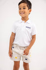 A smiling young boy wears a white Michigan polo shirt and “Michigan Critter Sheffield Shorts - Saratoga Stone” by The Beaufort Bonnet Company, decorated with multiple M logos, standing against a plain white background.