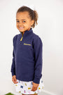A smiling young girl with curly hair is wearing The Beaufort Bonnet Company’s Michigan Hayword Half-Zip in Michigan Blue with Michigan Yellow, paired with a white skirt featuring colorful Michigan-themed prints, standing against a plain white background.