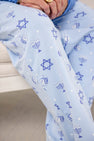 Men’s Sunday Style Sweatpants - Eight Nights to Remember by The Beaufort Bonnet Company are light blue pajama pants designed for holiday comfort, featuring Hanukkah-themed patterns such as Stars of David, menorahs, dreidels, and small white stars. Crafted in a style perfect for family matching, with a glimpse of the wearer’s hands and part of a chair visible.